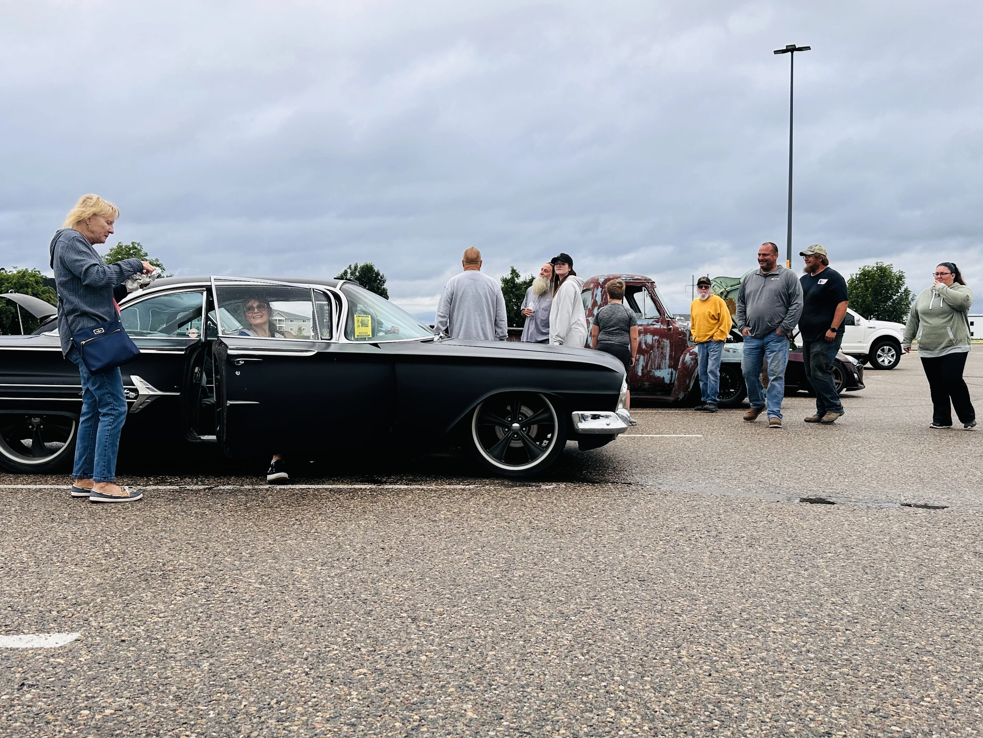 Low-angle shot of a slammed black classic car with people admiring it