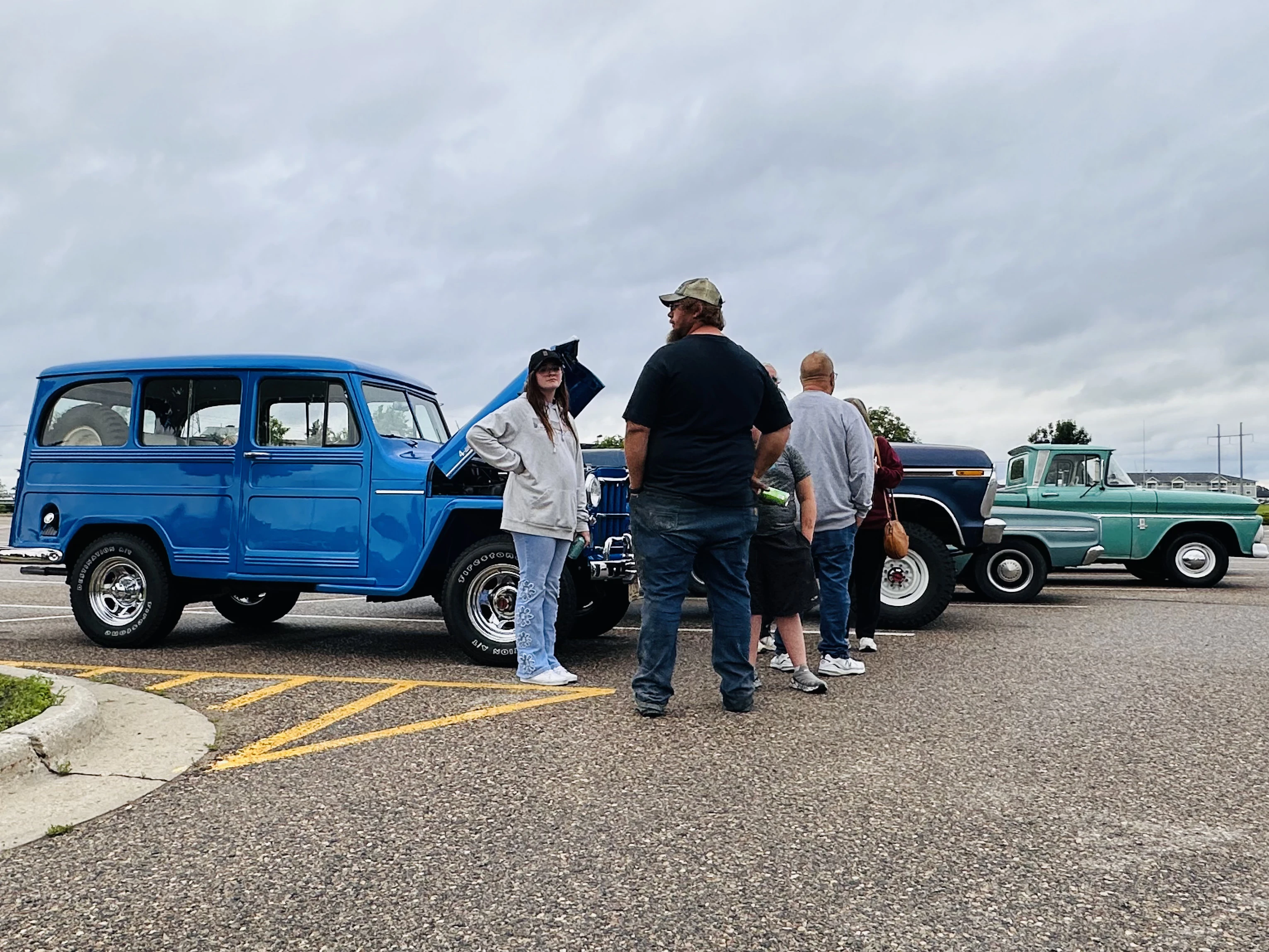 Bright blue Willys wagon and teal Chevy Apache truck with enthusiasts inspecting them