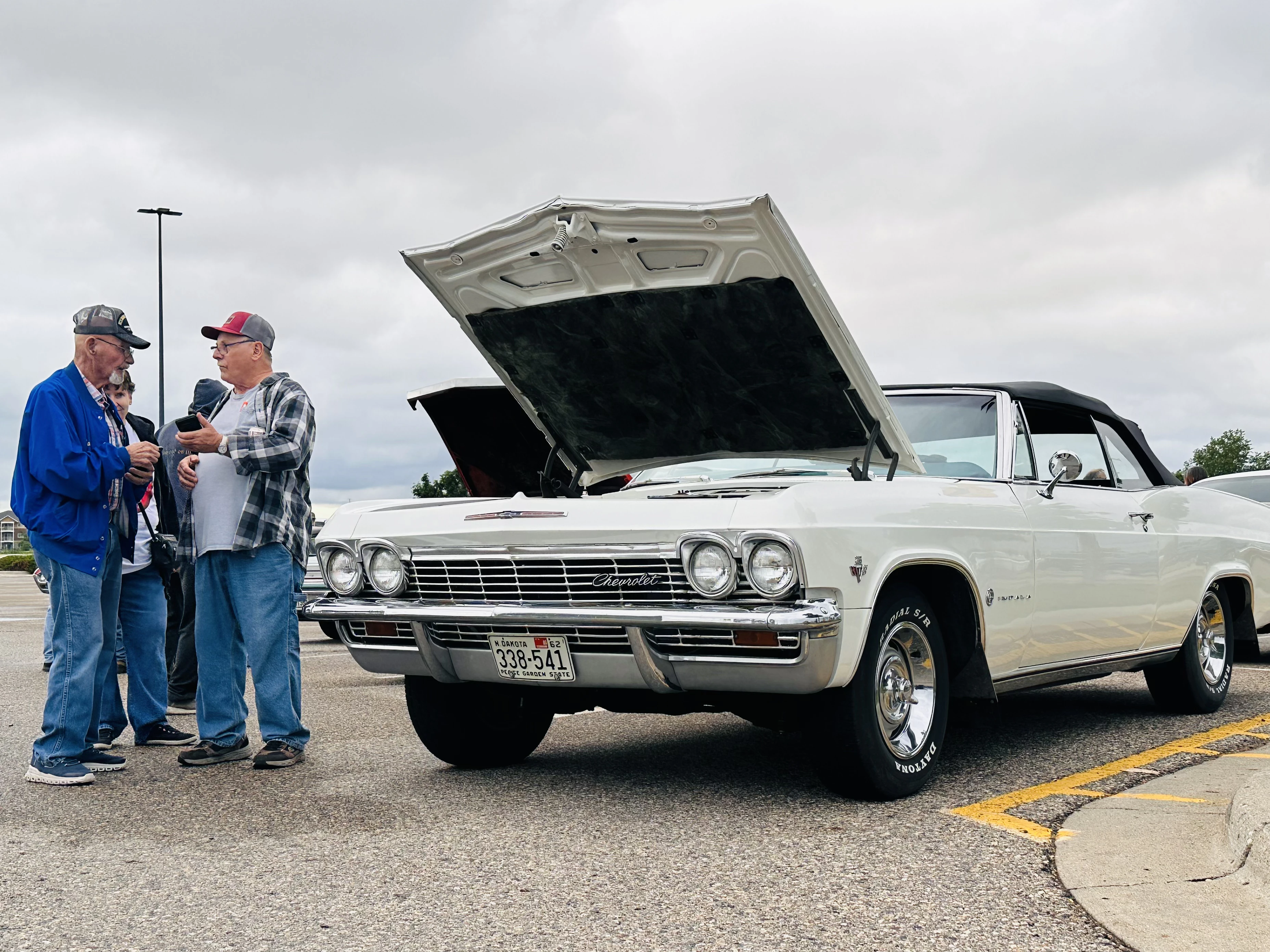White Chevrolet Impala convertible with hood up and owners chatting nearby