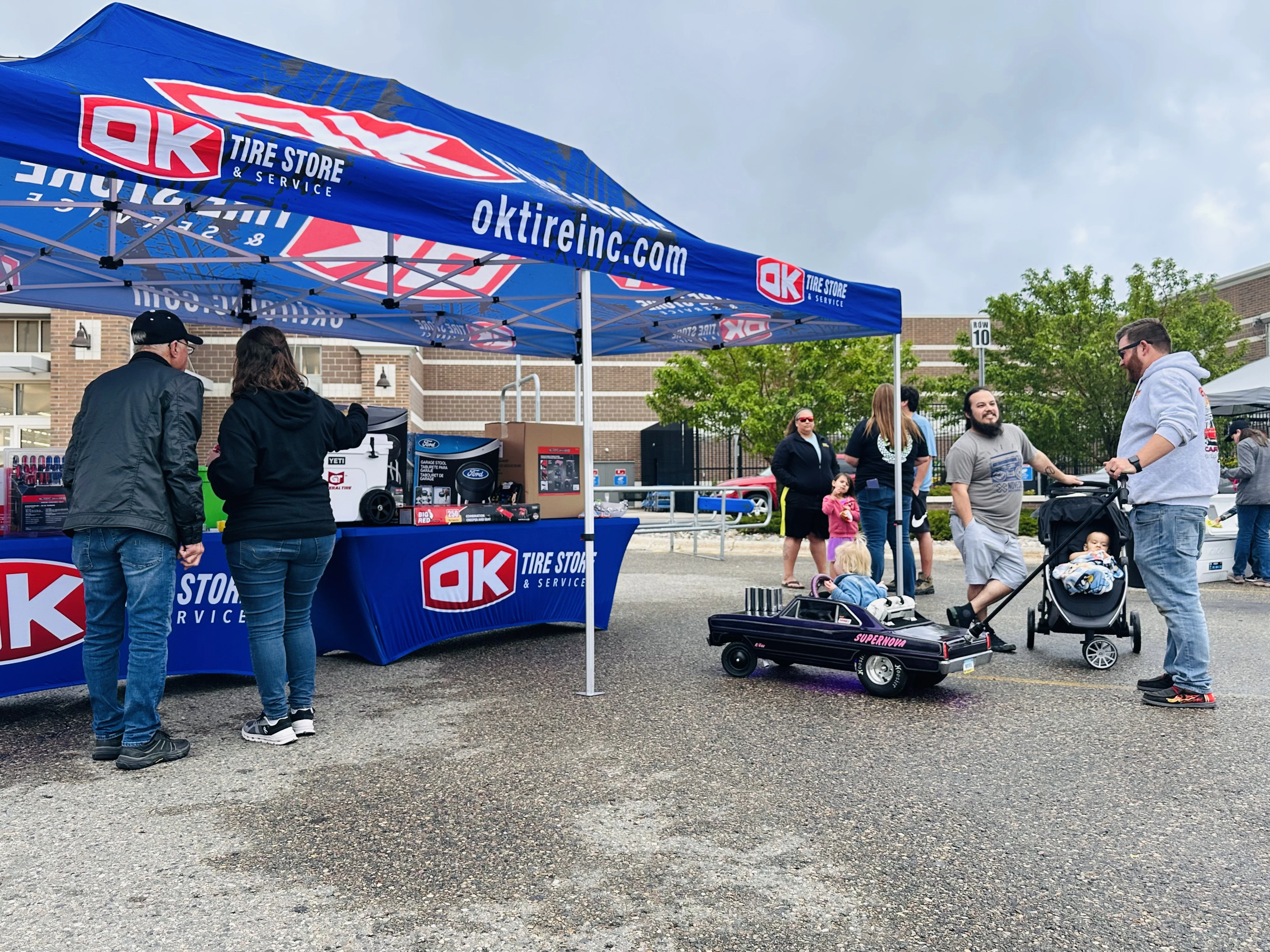 OK Tire branded tent with families and a child's pedal car at the event