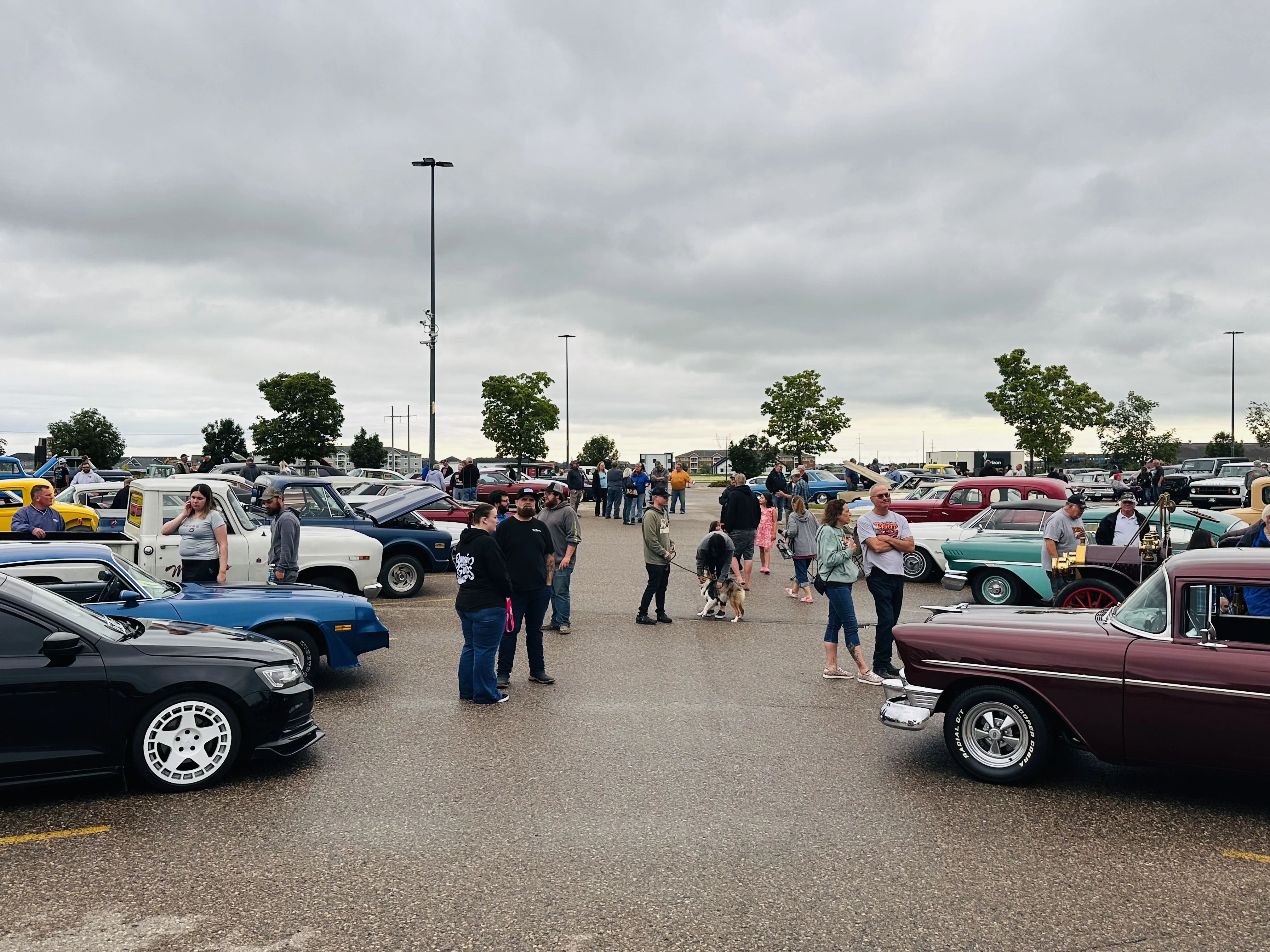 Rows of classic cars filling the Walmart parking lot with crowds of people walking between them at the OK Tire Round Up